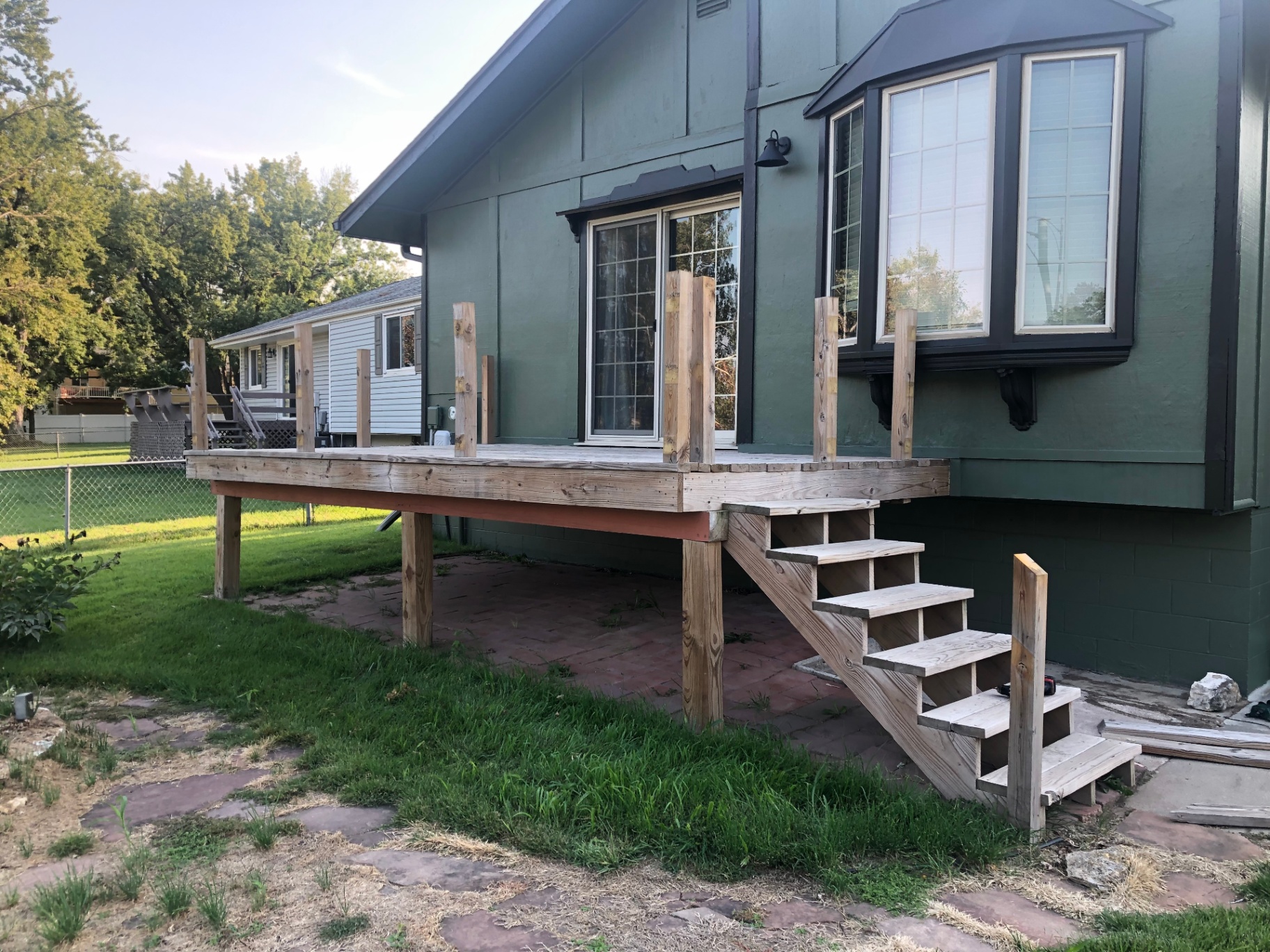 Deck framed and decked but not yet stained, with vertical railing posts and open stair stringers