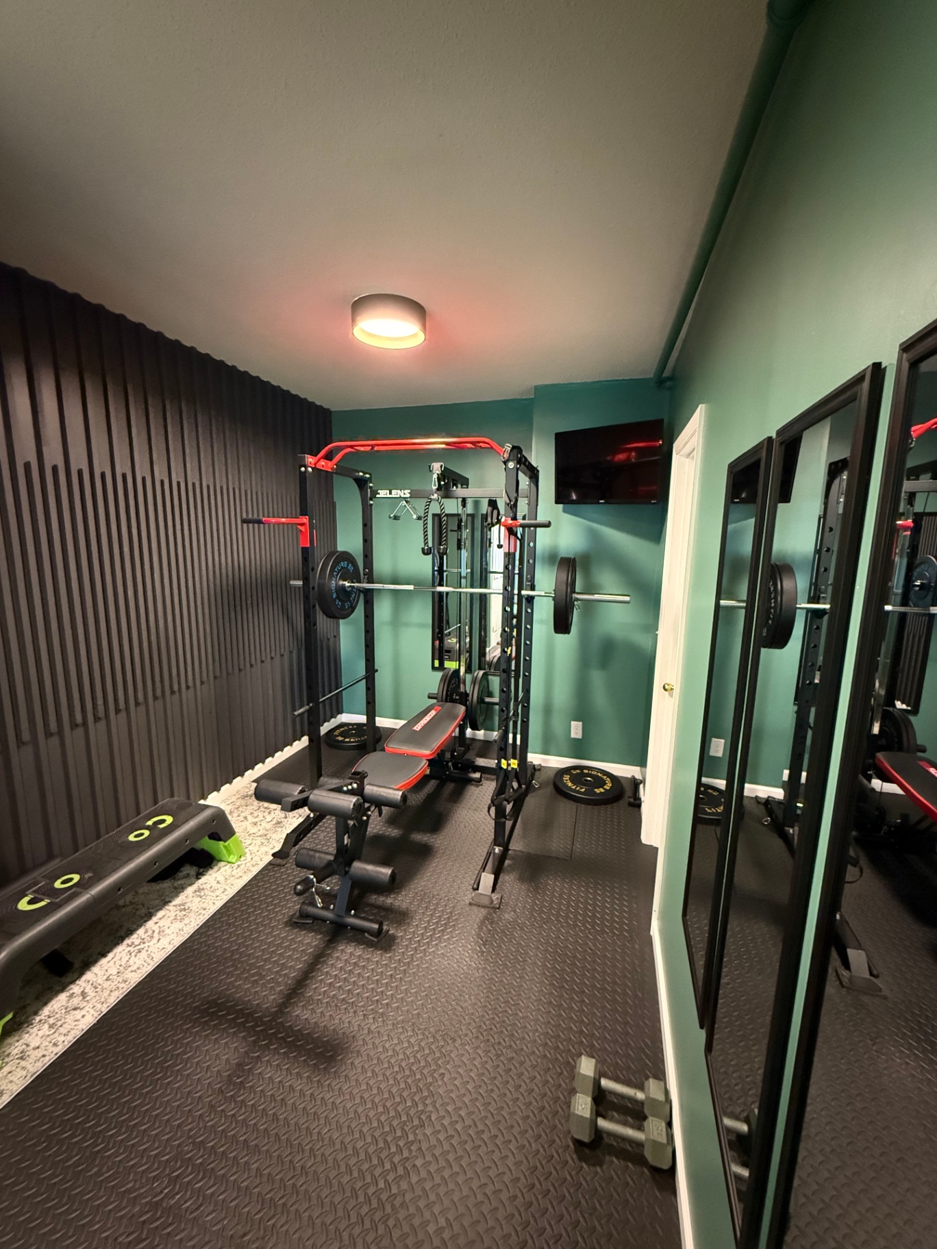 Finished home gym with a vertical black slat accent wall, teal painted walls, black rubber tile flooring, and full-length mirrors