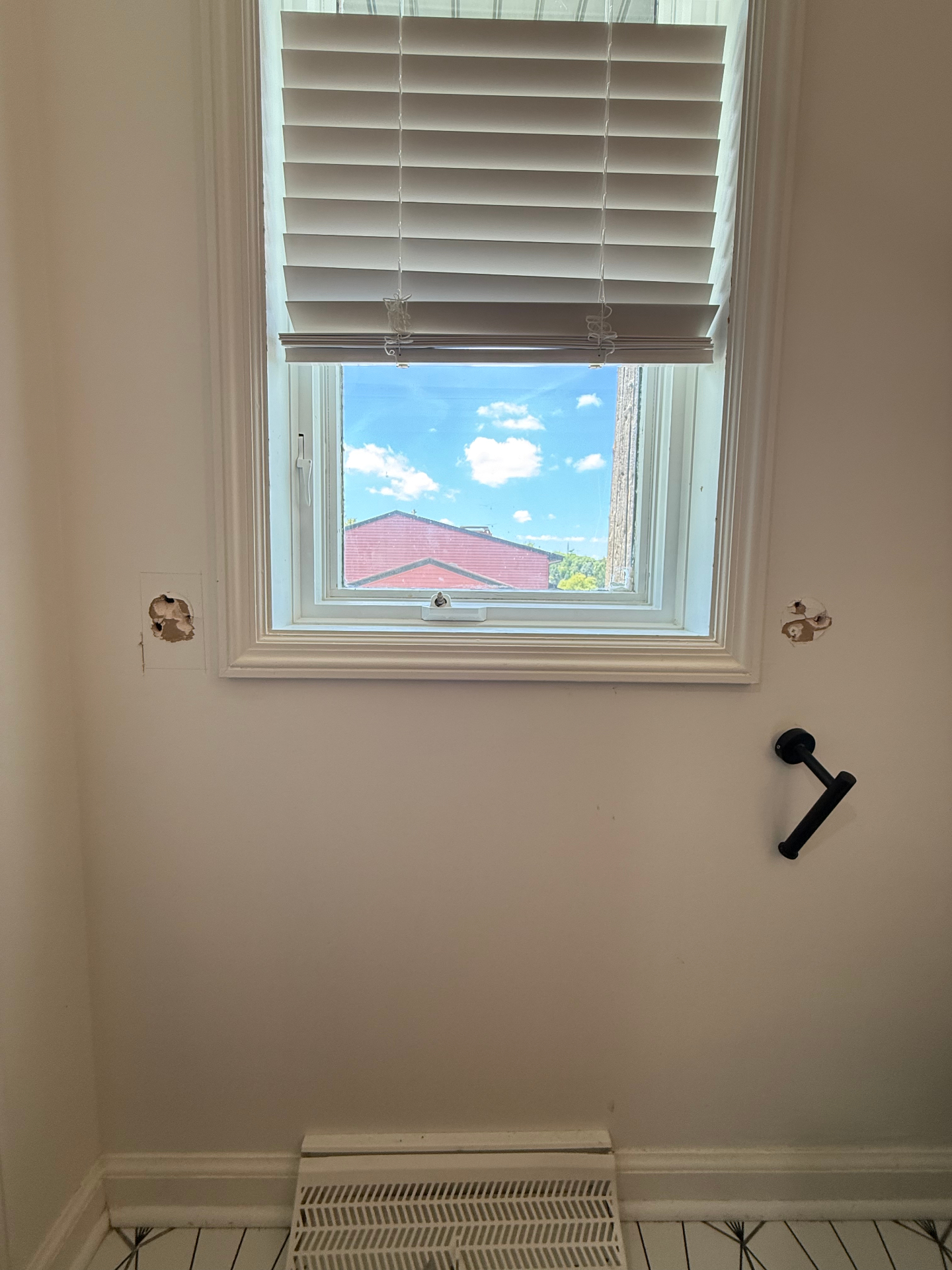 Bathroom wall next to a window before the grab bar was installed, with small openings where old hardware was removed