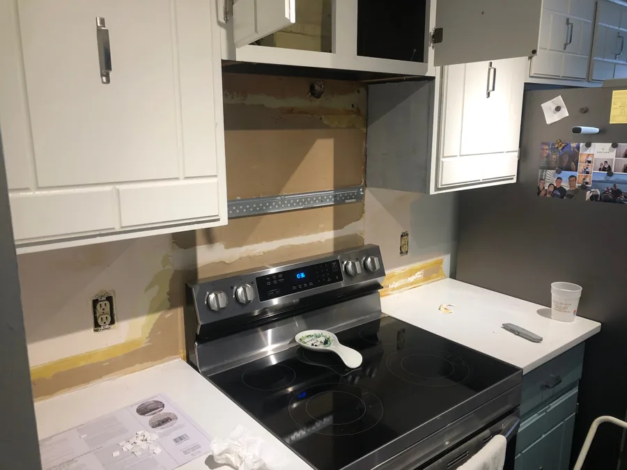 Kitchen wall with existing backsplash removed, exposing patched drywall and mounting points behind the range
