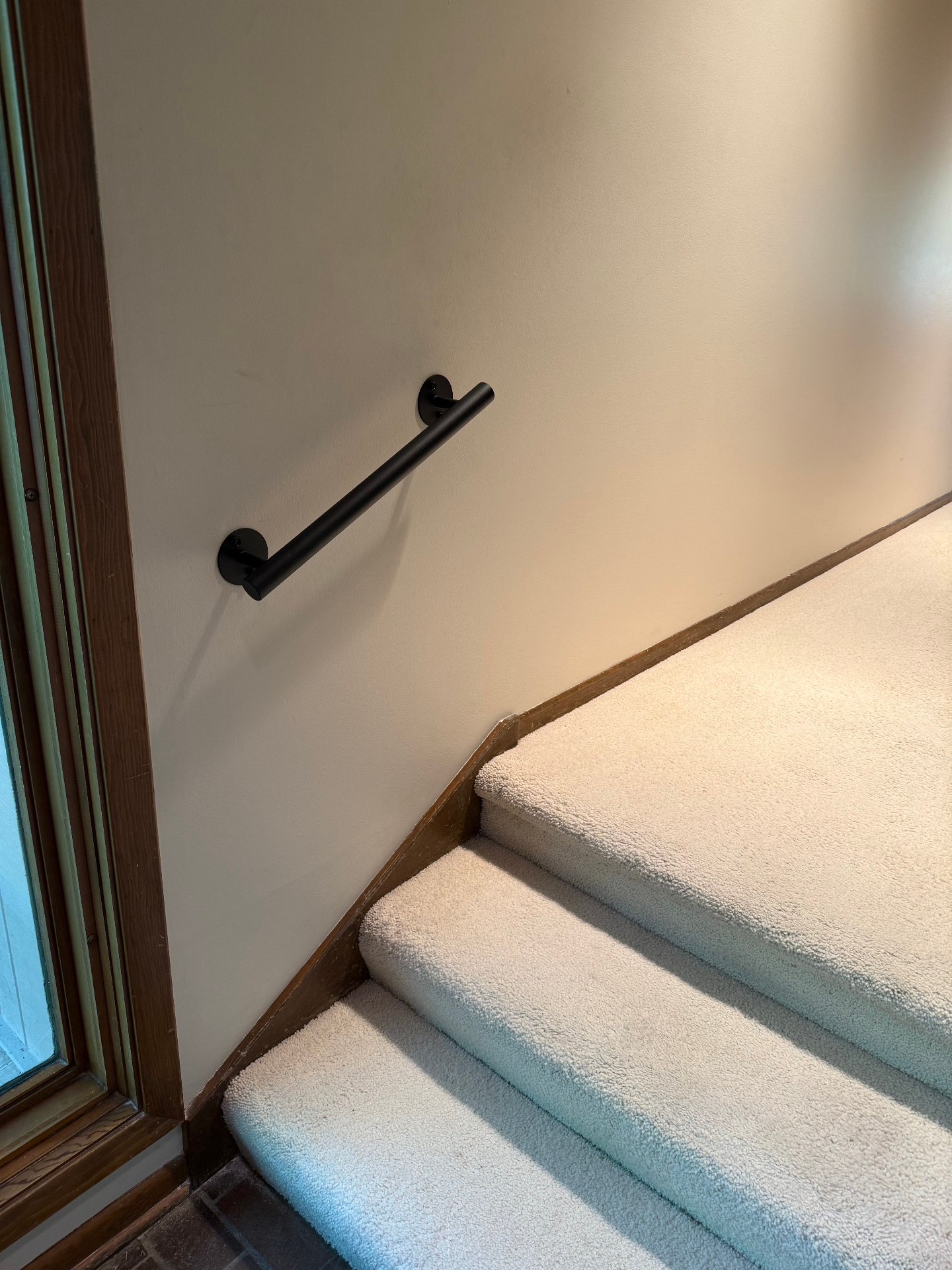 Matte black metal handrail installed along a carpeted interior stairway wall