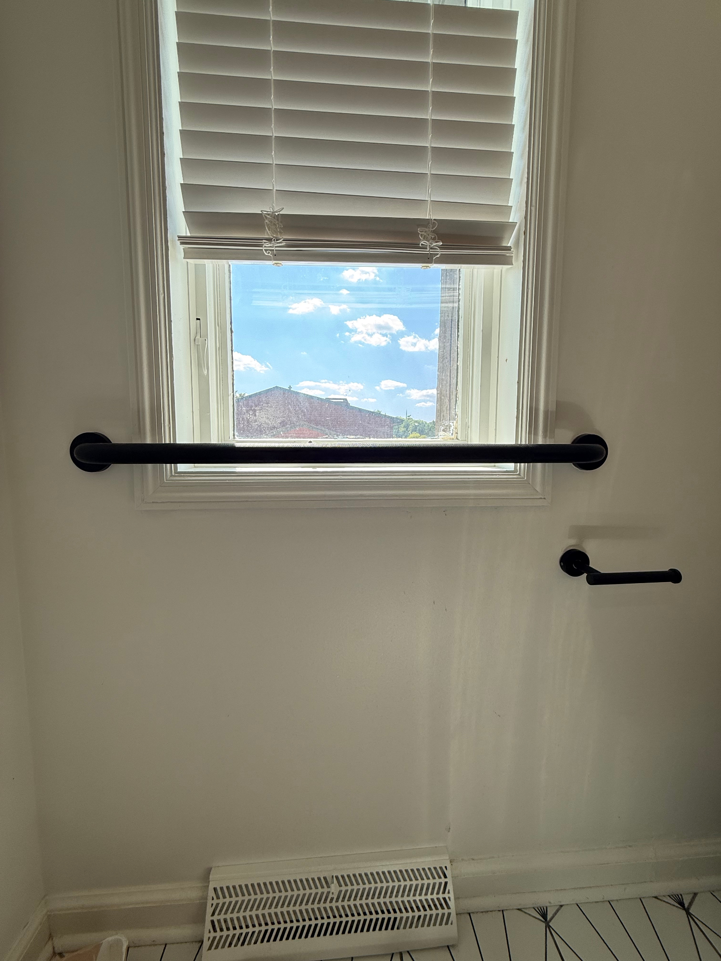 Matte black bathroom grab bar mounted horizontally under a window with a matching toilet paper holder
