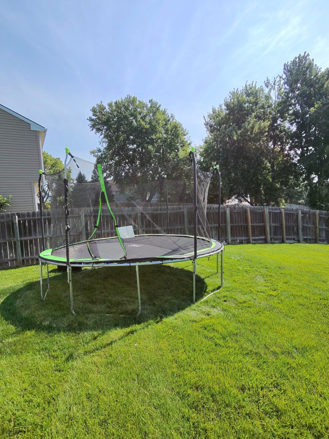 Fully reassembled large green and black backyard trampoline with safety enclosure at the new location