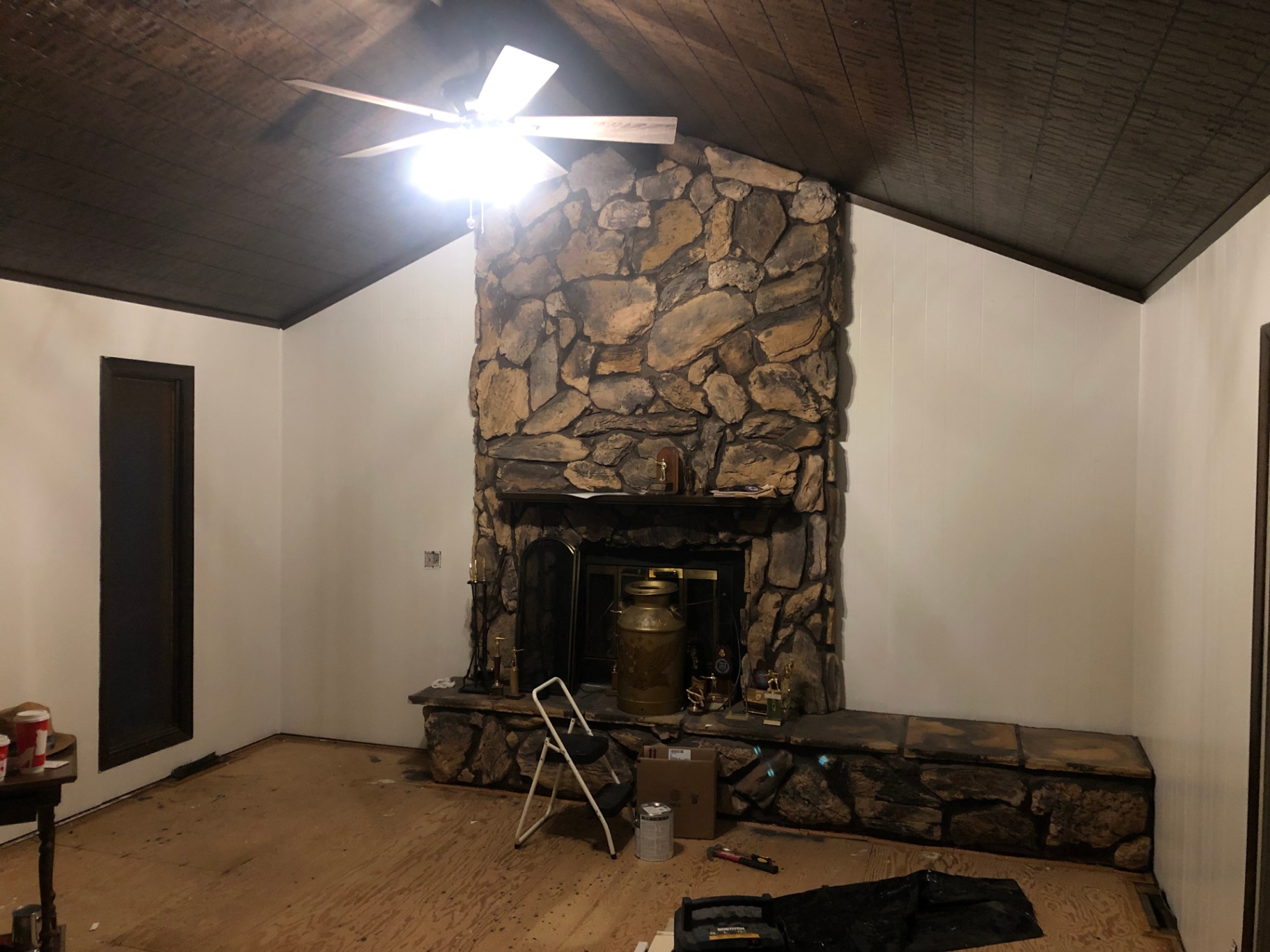 Living room with dark wood paneling repainted crisp white around the original floor-to-ceiling stone fireplace