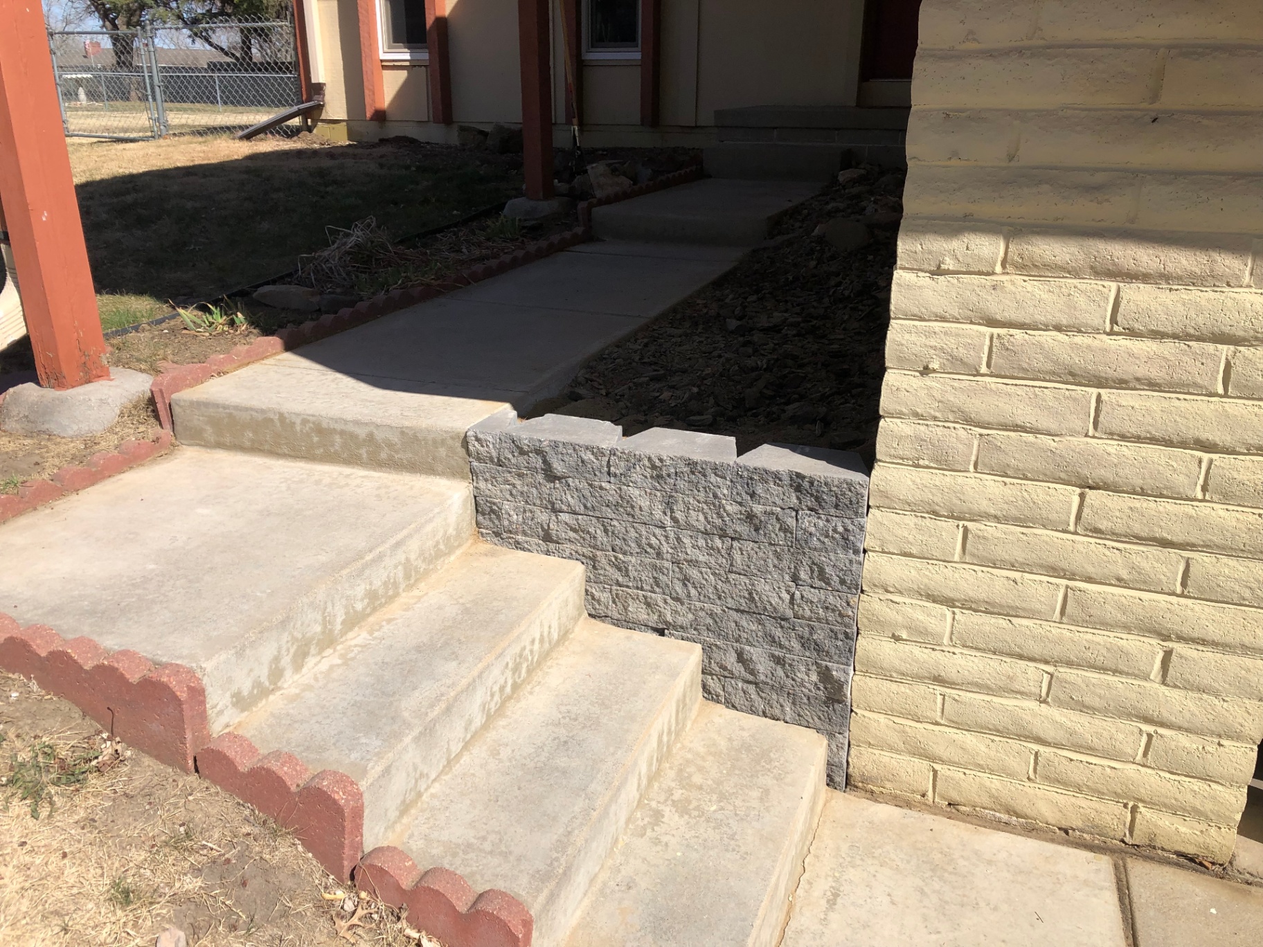 Front concrete steps with a new gray stacked-block retaining wall replacing the old loose stone stack