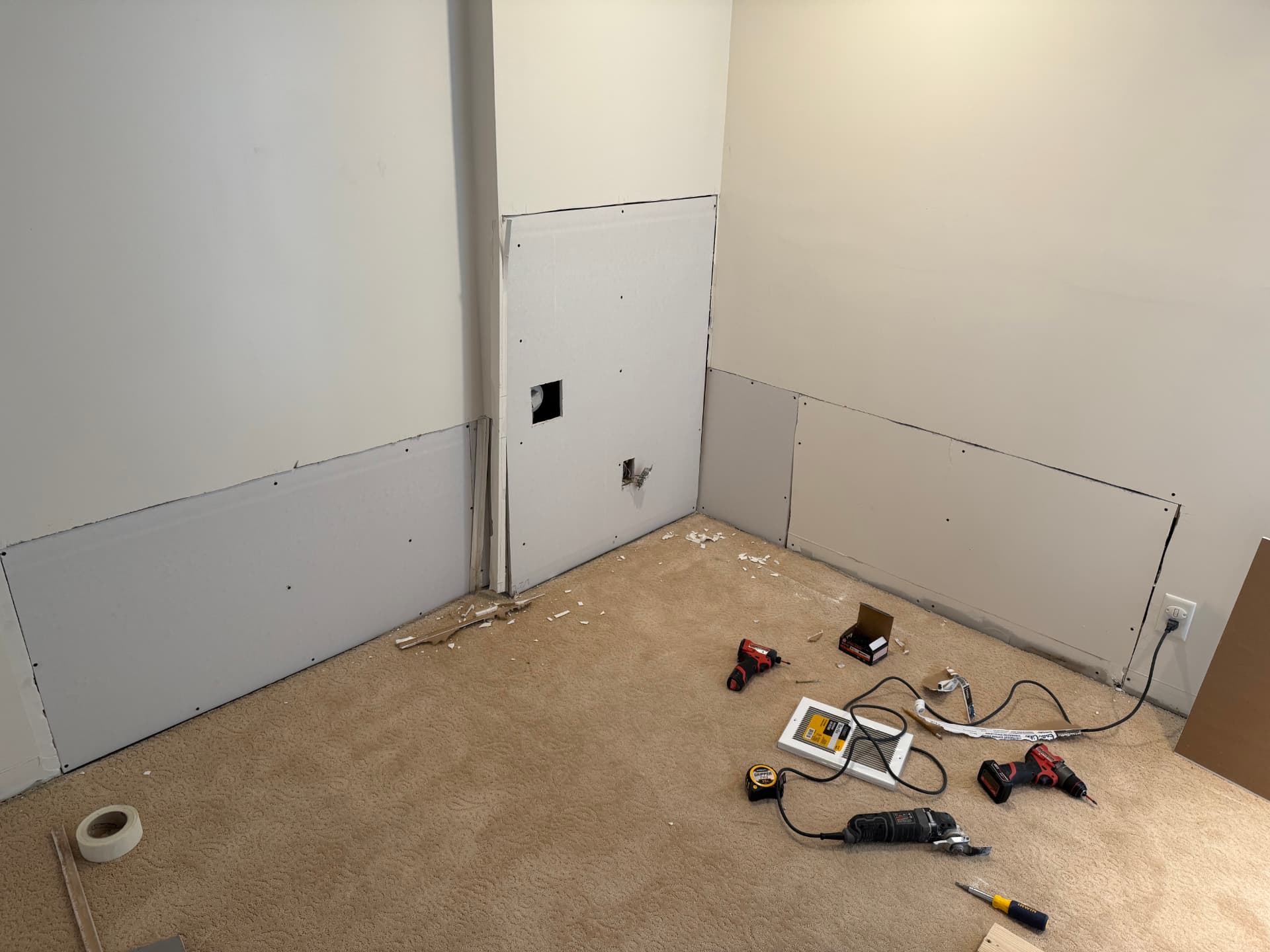 Two-Tone Blue Interior Paint before: unpainted room with drywall patches, exposed outlet, and tools on the carpet