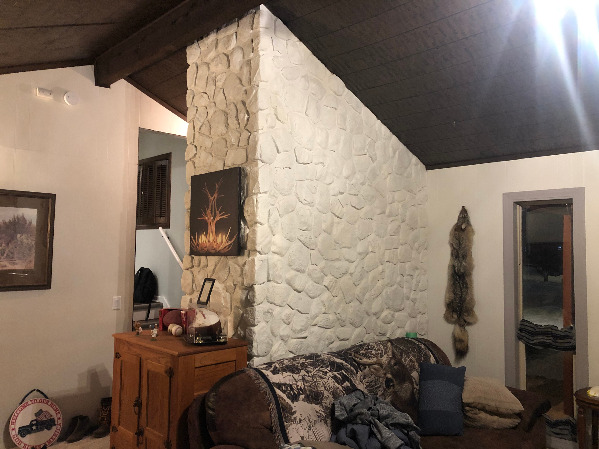 Full-height interior stone accent wall painted a clean white, next to painted wood-paneled walls and a dark wood plank ceiling